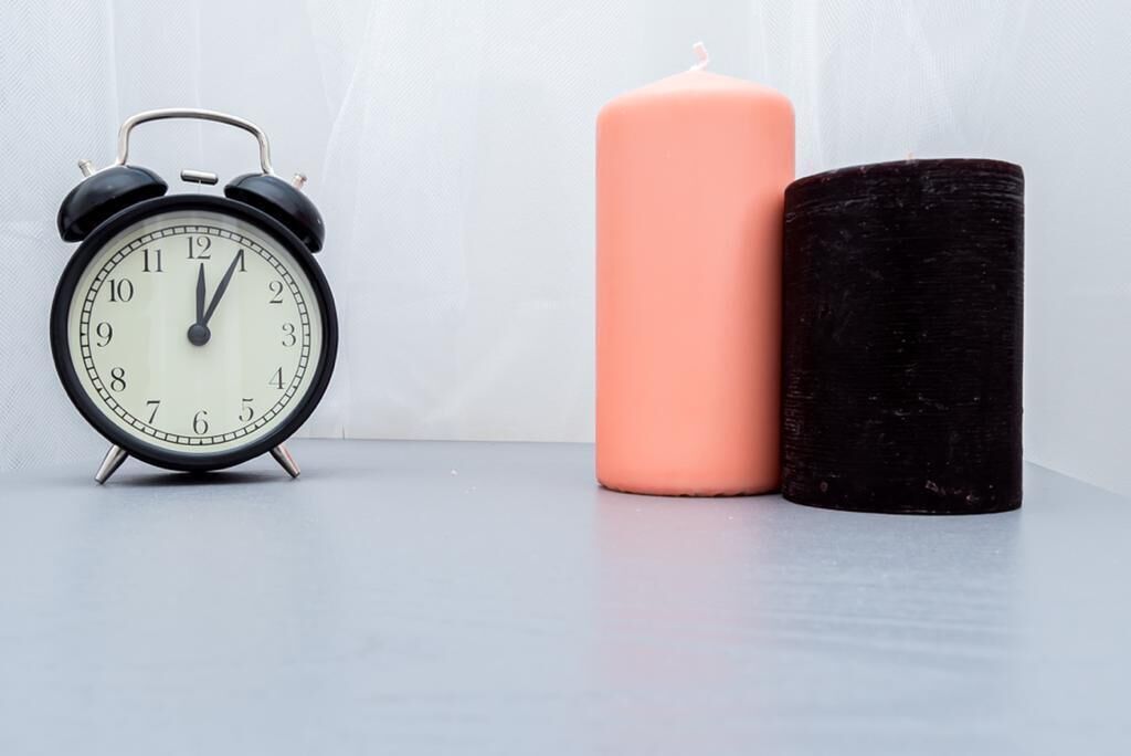 A black analog alarm clock and a pink candle on a table.