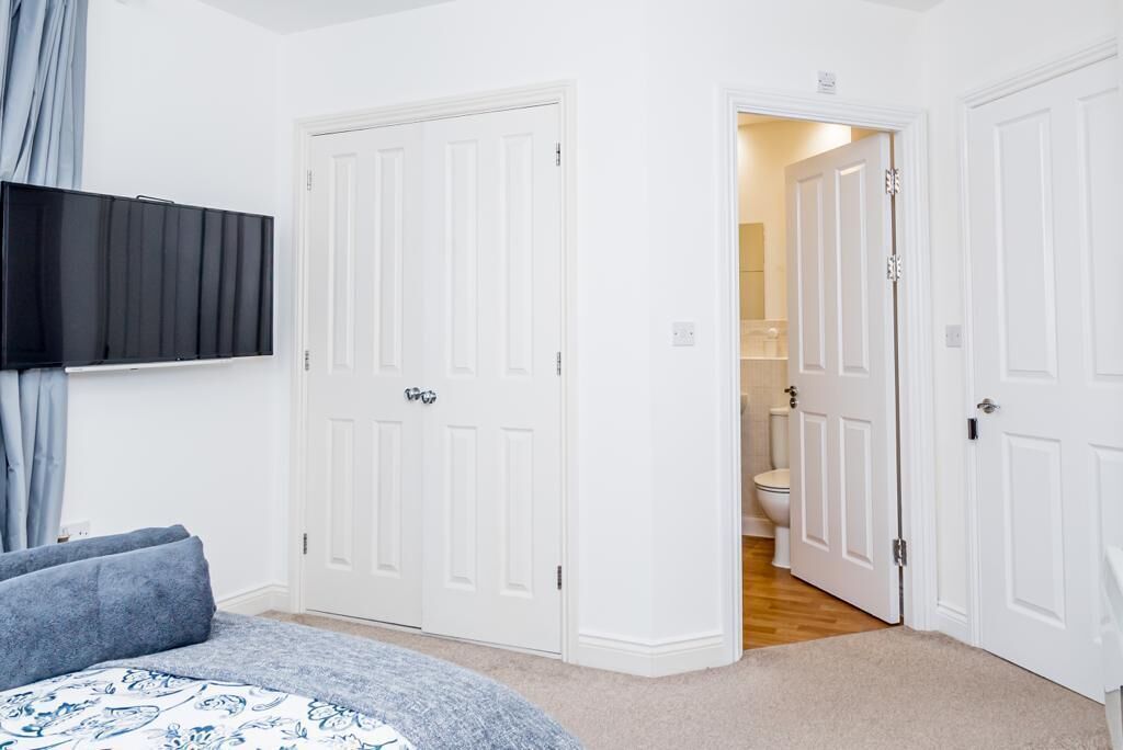 A bedroom with a bed, a TV mounted on the wall, and white doors leading to other rooms.