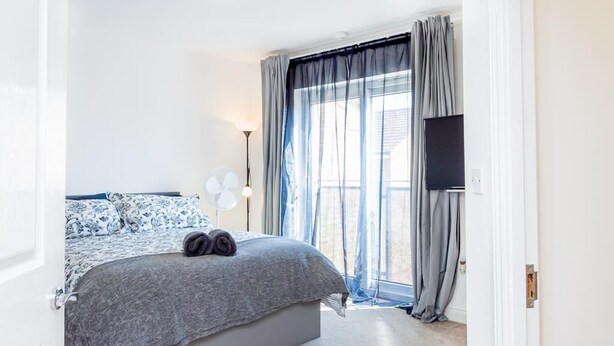 A bedroom with a bed, a TV, and a window with curtains. - Bayview Apartments (Southampton)