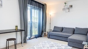 A modern living room with a grey sofa, a small table, a chair, and a large window with curtains. - Bayview Apartments (Southampton)