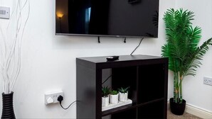 A modern living room with a flat-screen TV mounted on the wall, a dark wooden entertainment unit below, and a potted plant to the right. - Bayview Apartments (Southampton)