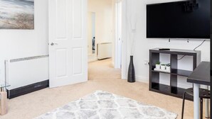 A modern living room with a large flat-screen TV, a black entertainment unit, and a white door leading to another room. - Bayview Apartments (Southampton)