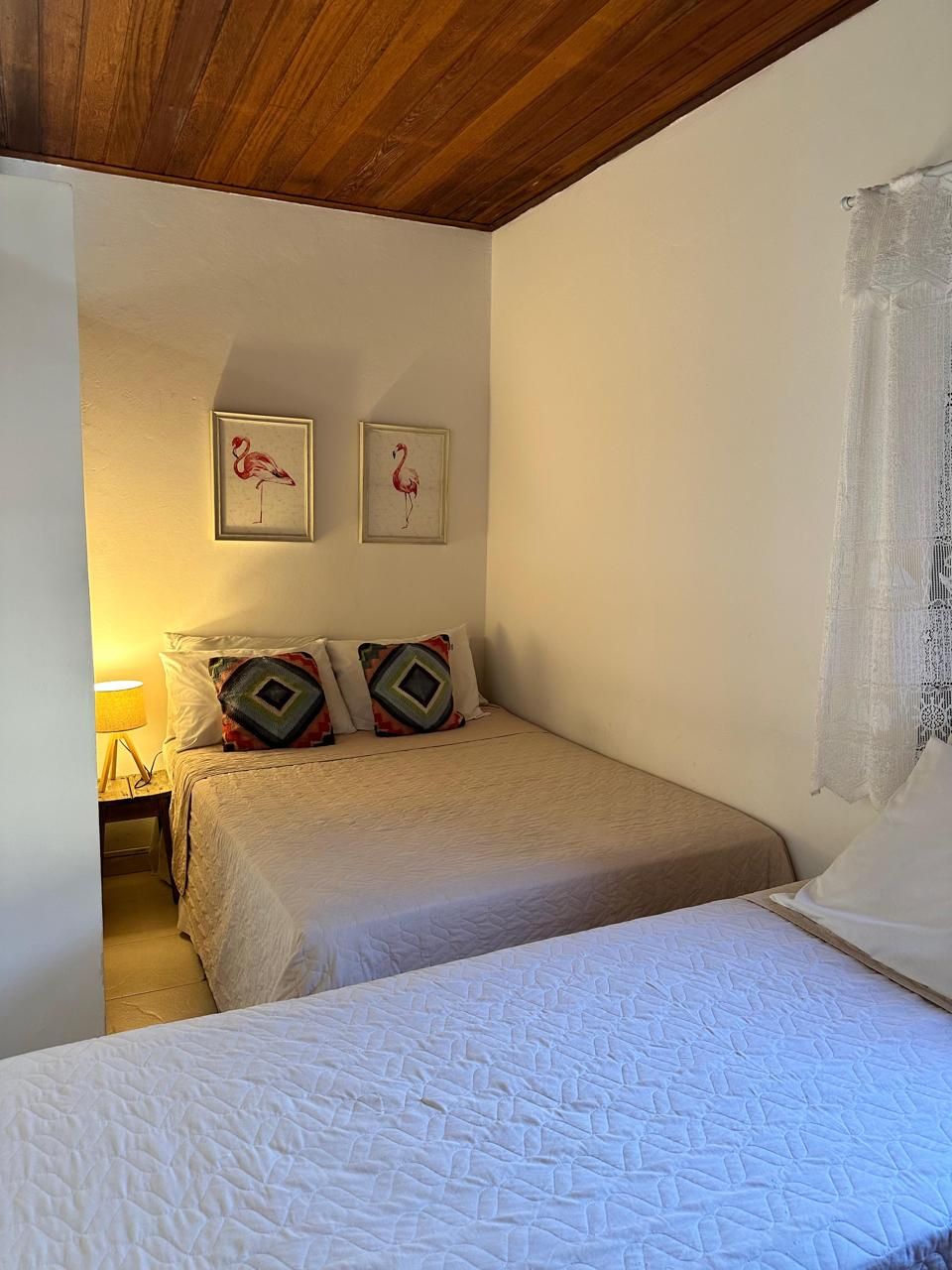 A bedroom with two beds, a wooden ceiling, and two framed flamingo pictures on the wall.