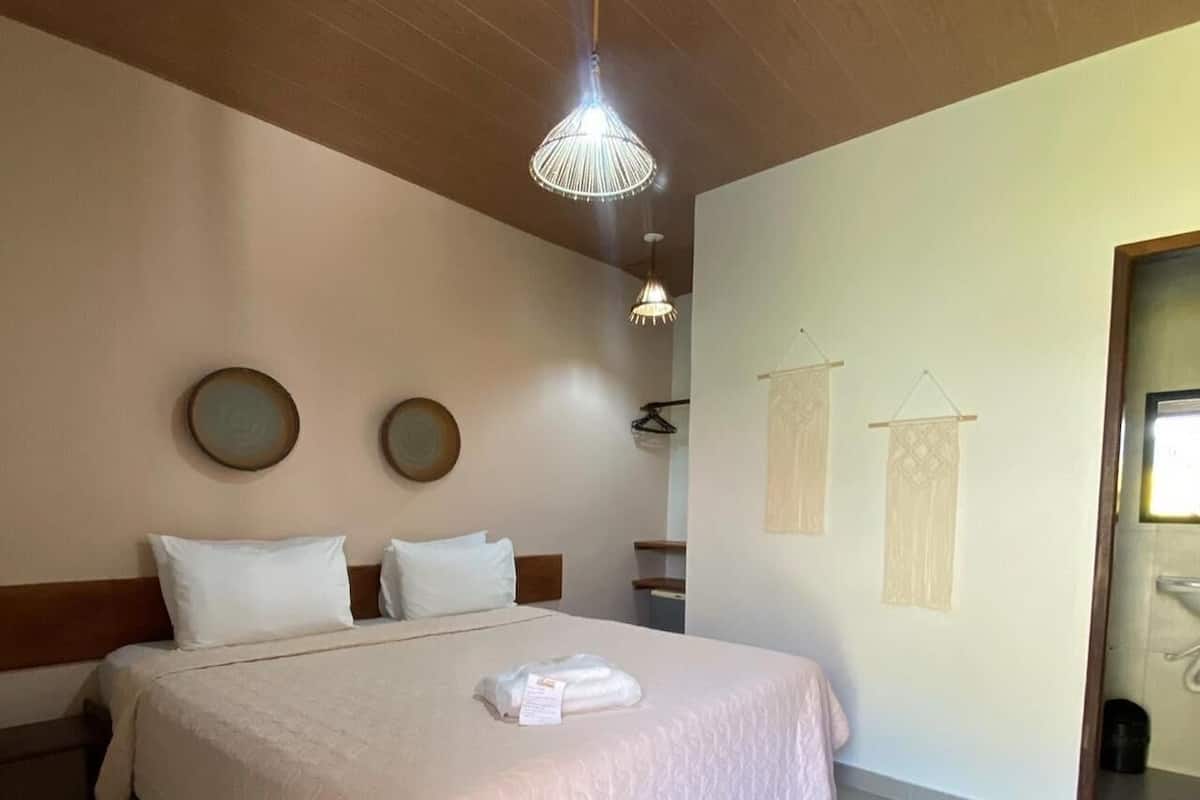 Ein ordentlich bezogenes Bett mit weißer Decke und Kissen, ein Holz-Kopfteil, eine hängende Leuchte und ein kleiner Teppich auf dem Boden.