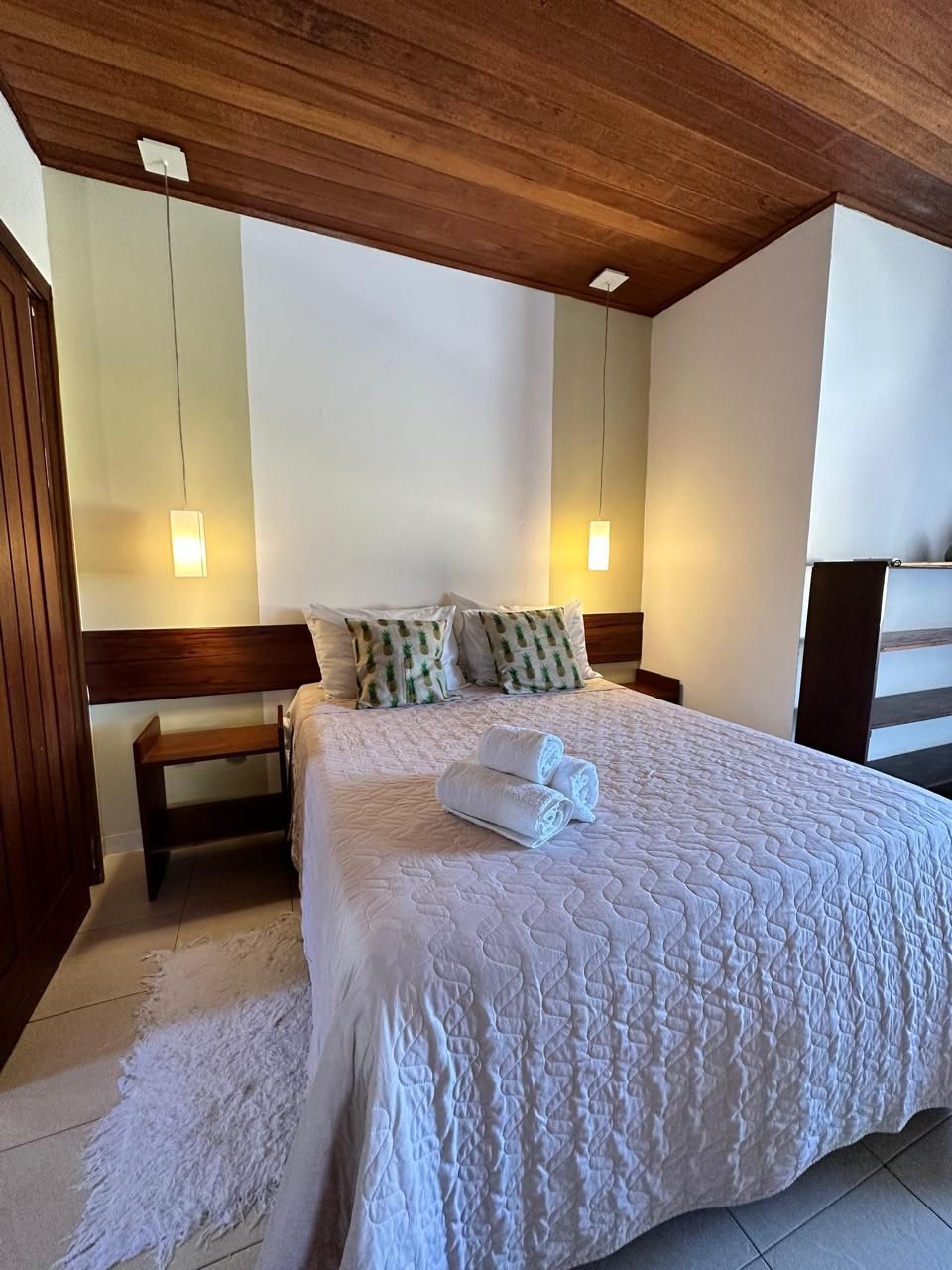 A neatly made bed with white bedding and rolled towels, a wooden headboard, and a small bedside table.