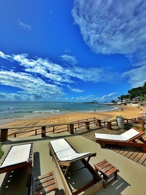 Un patio frente a la playa con sillones de madera y vistas al océano.