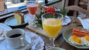 Ett bord dukat med frukosttillbehör, inklusive äggröra, rostat bröd, ett glas apelsinjuice, en kopp kaffe och en bit tårta, med utsikt över stranden och havet genom stora fönster.