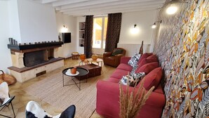 Een woonkamer met een open haard, een zithoek, een salontafel en een behang met een patroon.