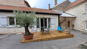 Een binnenplaats met een houten terras, een pot met een olijfboom, tuinmeubels en een trap naar een hoger gelegen niveau.