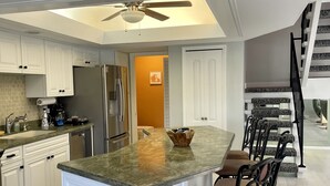 A modern kitchen with white cabinetry, a central island with bar stools, a stainless steel refrigerator, and a ceiling fan. - Waterfront Spanish Villa with private pool and lake views - 5 mins from beach! (Bonita Springs)