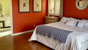 A bedroom with a bed, wooden floor, ceiling fan, framed pictures, and a window with blinds. - Waterfront Spanish Villa with private pool and lake views - 5 mins from beach! (Bonita Springs)