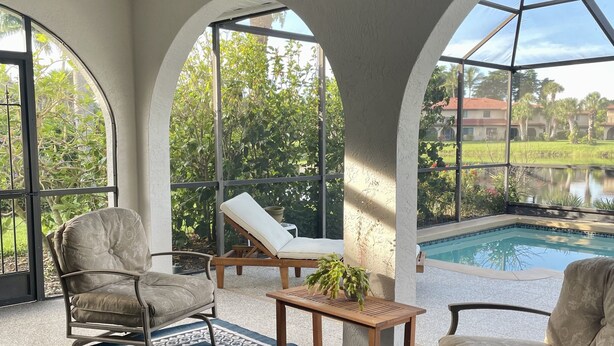 A sunlit patio with a pool, two lounge chairs, a table with a plant, and a ceiling fan. - Waterfront Spanish Villa with private pool and lake views - 5 mins from beach! (Bonita Springs)