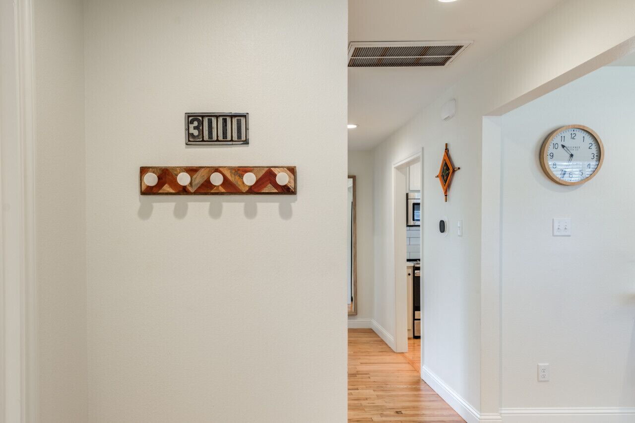 A hallway with a wooden floor, a clock on the right wall, and a door at the end.