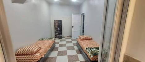 A narrow hallway with two beds on either side, checkered floor tiles, and a door at the end.