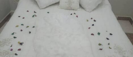 Un lit recouvert d’une couverture blanche, orné de plusieurs oreillers et parsemé de feuilles colorées.