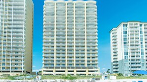 Un hôtel à plusieurs étages, à l’architecture extérieure uniforme, doté de balcons et surplombant un ciel d’un bleu limpide.