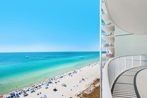 A beachfront hotel with a curved balcony overlooking a sandy beach and turquoise waters.