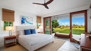 A bedroom with a large bed, a ceiling fan, and a view of a golf course through the sliding glass door.