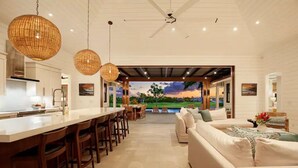 A modern kitchen with a bar area, a dining set, and a living area with a sofa and a view of a landscape through a large window.