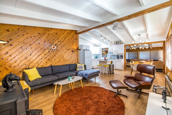 A modern living space with a wooden ceiling, a sofa, a coffee table, a leather chair, and a kitchen area with white cabinets and a microwave.