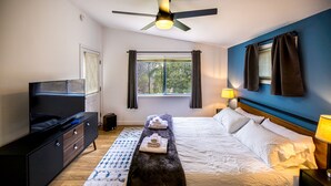 Een slaapkamer met een bed, nachtkastje, lamp, televisie en een plafondventilator.