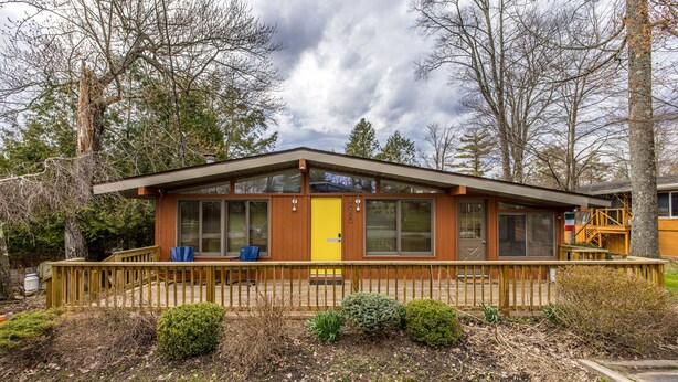 Een modern gelijkvloers huis met een houten terras, grote ramen en een gele deur.