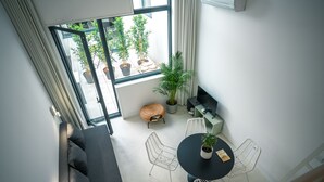 A modern living room with a sofa, a round table with chairs, a potted plant, and a view of the outside through a large window. - Portaria Housing (Aveiro)