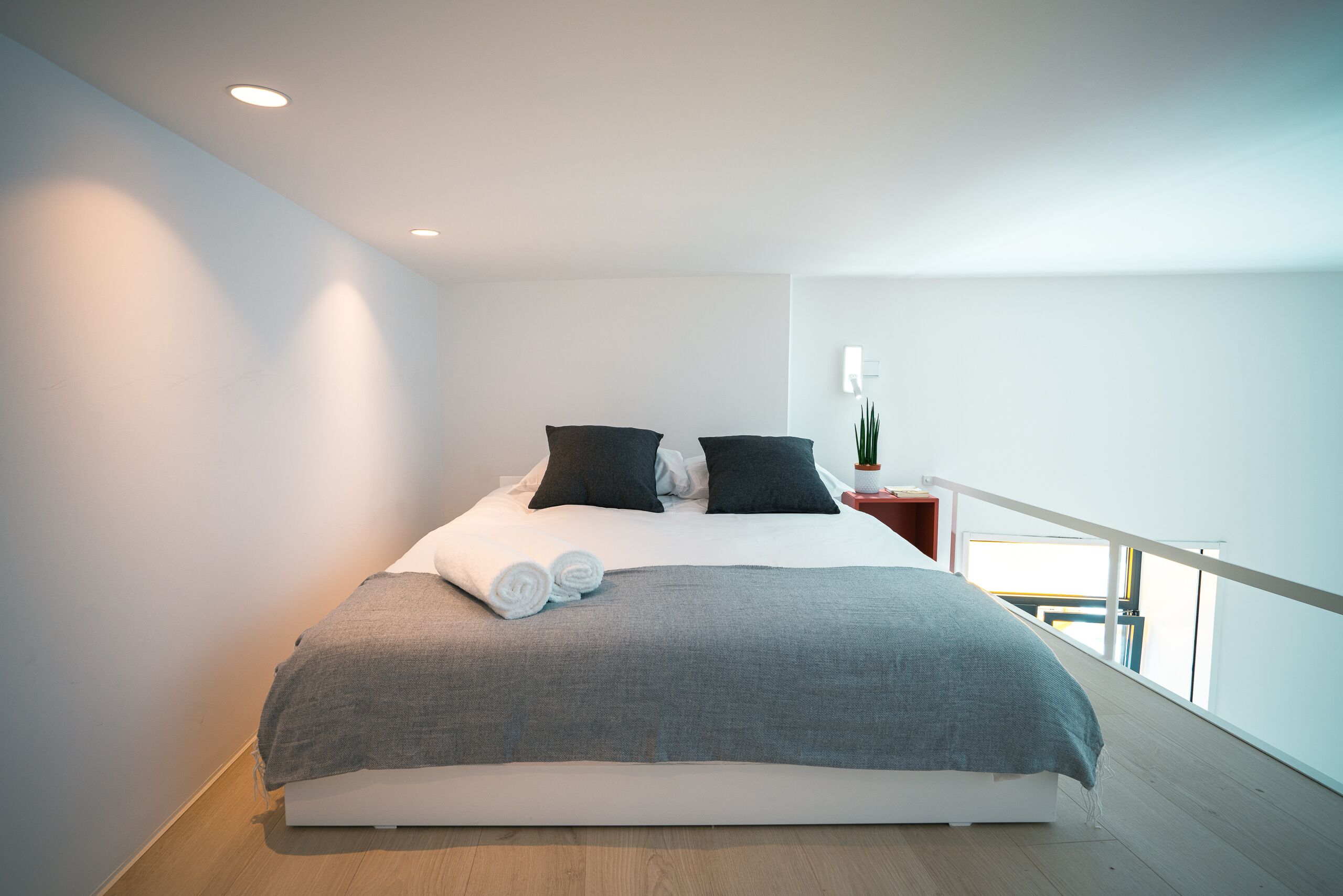 A modern bedroom with a large bed, a nightstand, and a potted plant.