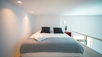 A modern bedroom with a large bed, a nightstand, and a potted plant.