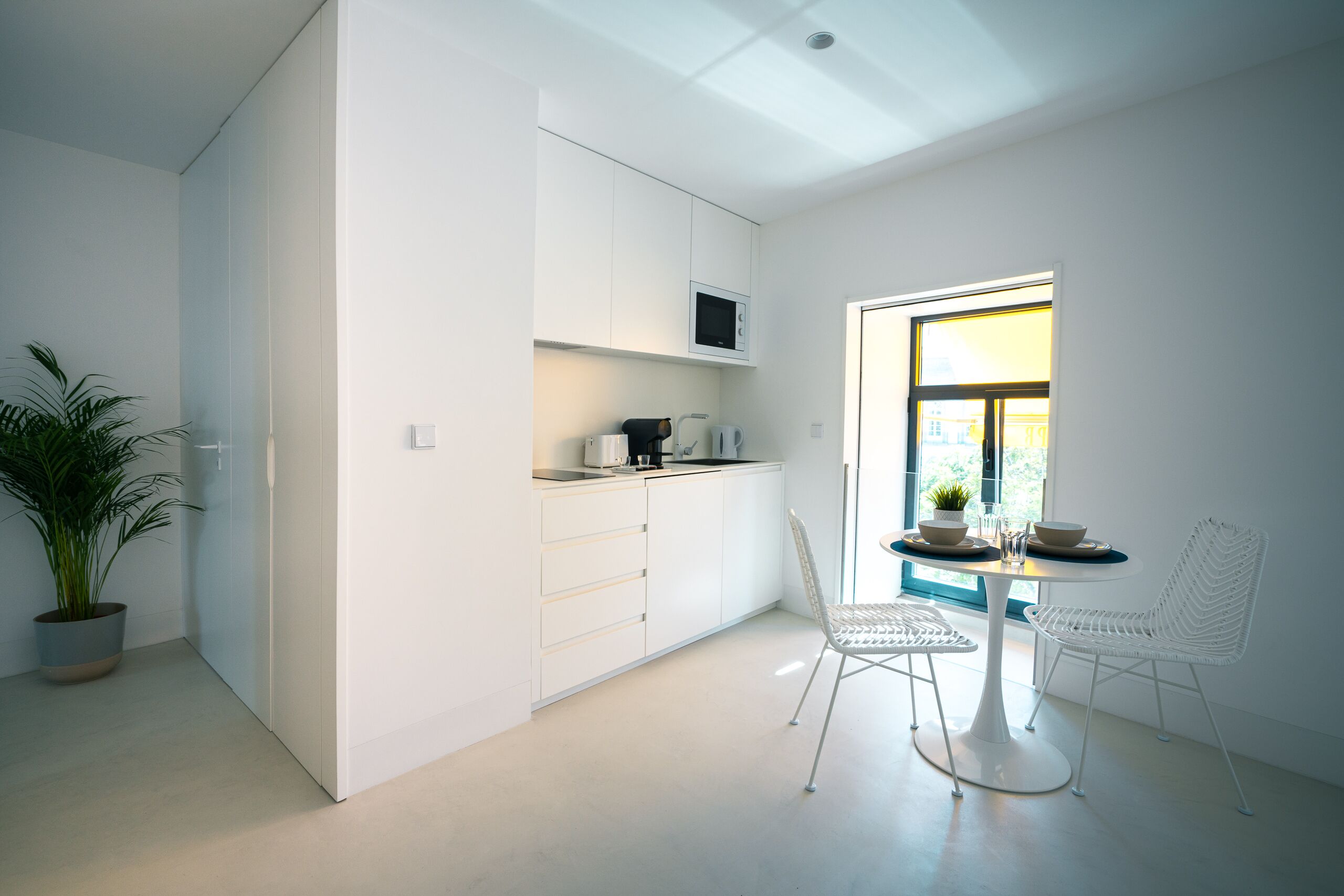 Une cuisine moderne avec des meubles blancs, un four à micro-ondes et un coin repas comprenant une table et des chaises blanches.