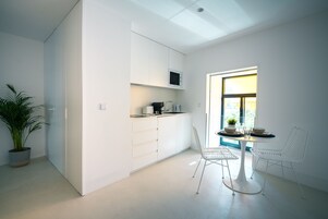 Una cocina moderna con armarios blancos, un microondas y una zona de comedor con una mesa y sillas blancas.