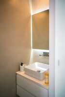 Un baño con un lavamanos blanco, un espejo y una botella de jabón de manos en la encimera.