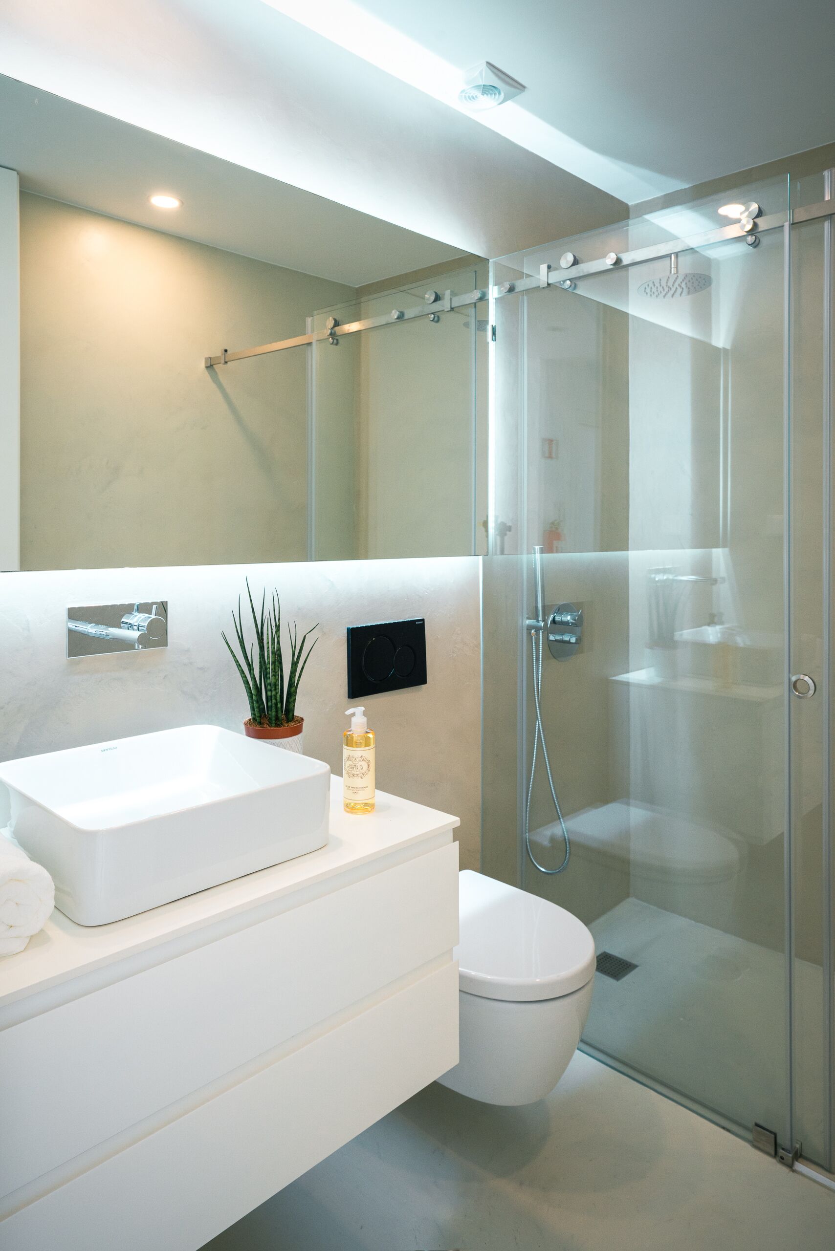 Un baño moderno con ducha envuelta en vidrio, un lavamanos blanco y un inodoro.