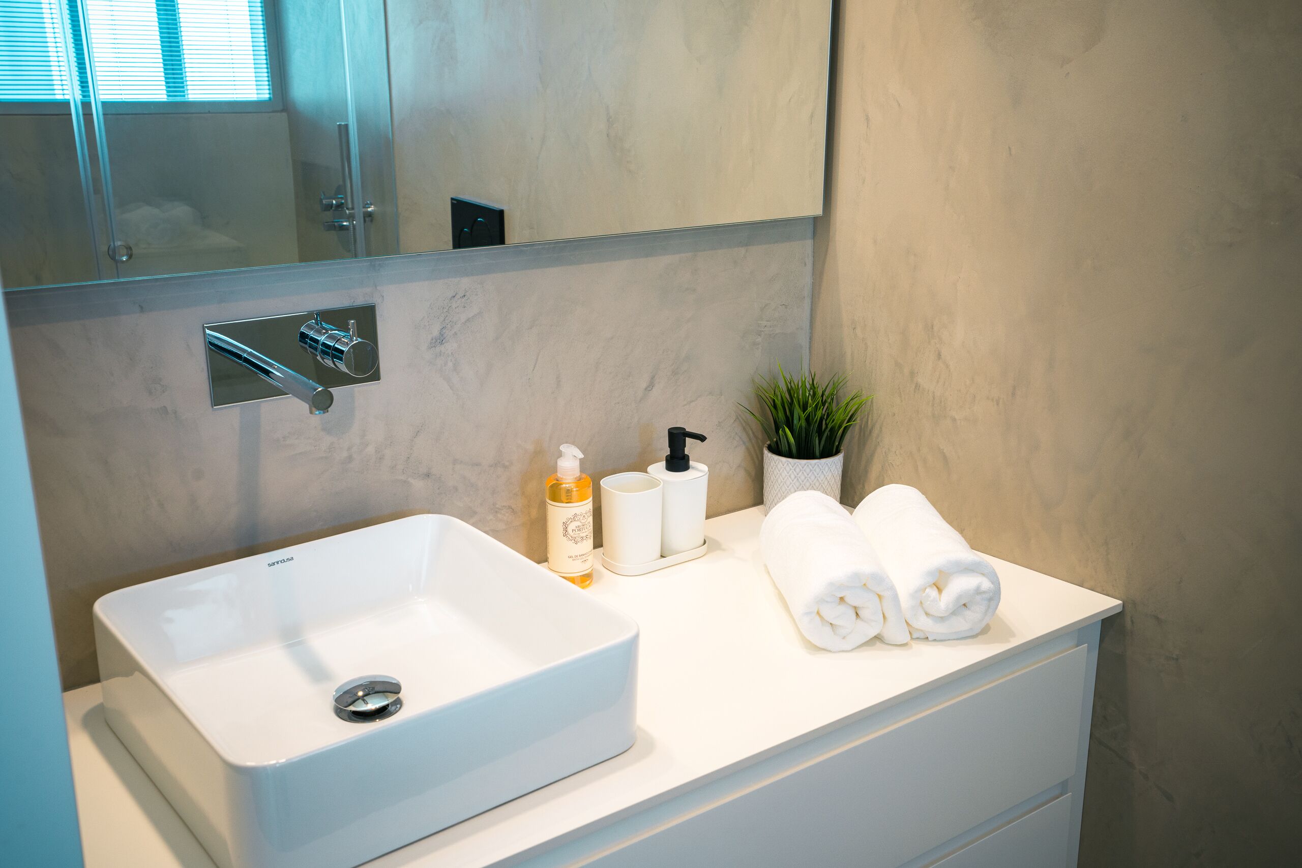 Un baño con un lavabo blanco, un espejo, una toalla y una pequeña planta en maceta.
