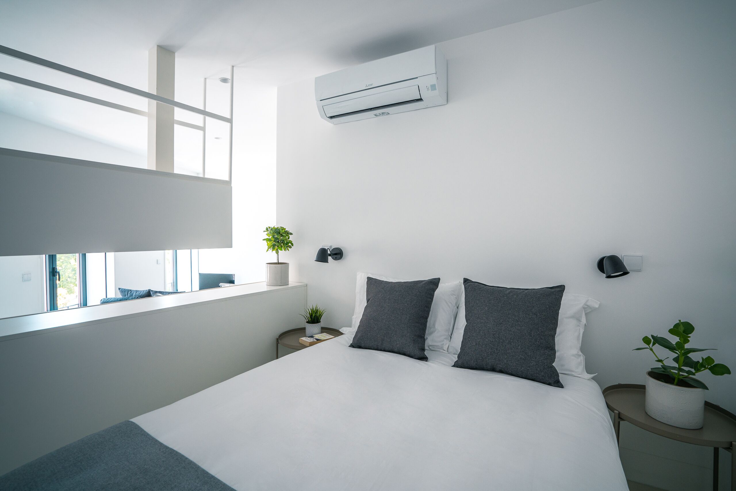 A modern bedroom with a large bed, bedside tables, a window, and an air conditioning unit.