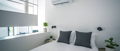 A modern bedroom with a large bed, bedside tables, a window, and an air conditioning unit.