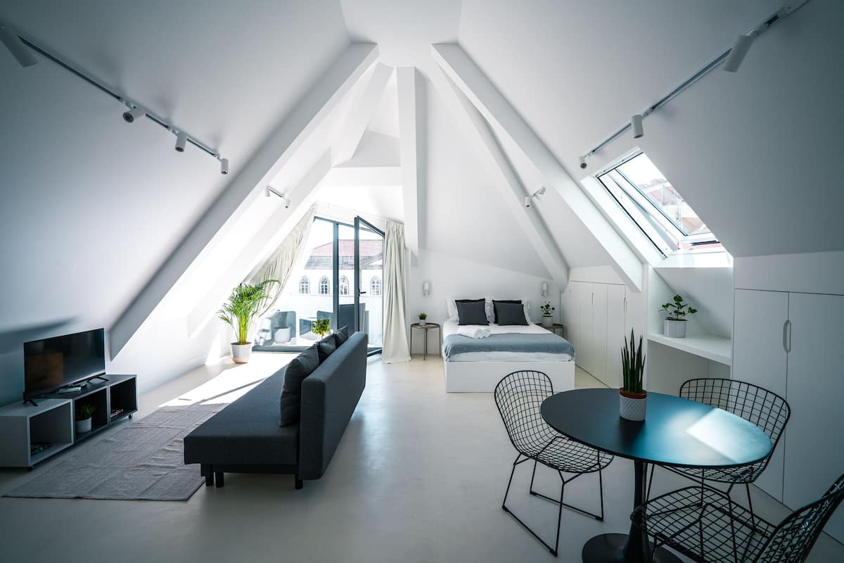 En modern lägenhet i loftstil med högt tak, takfönster, ett vardagsrum med soffa och TV, en matplats med bord och stolar samt ett sovrum med säng och sängbord.