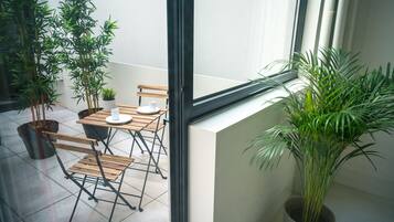 Un balcón con mesa y sillas, plantas en macetas y una ventana.