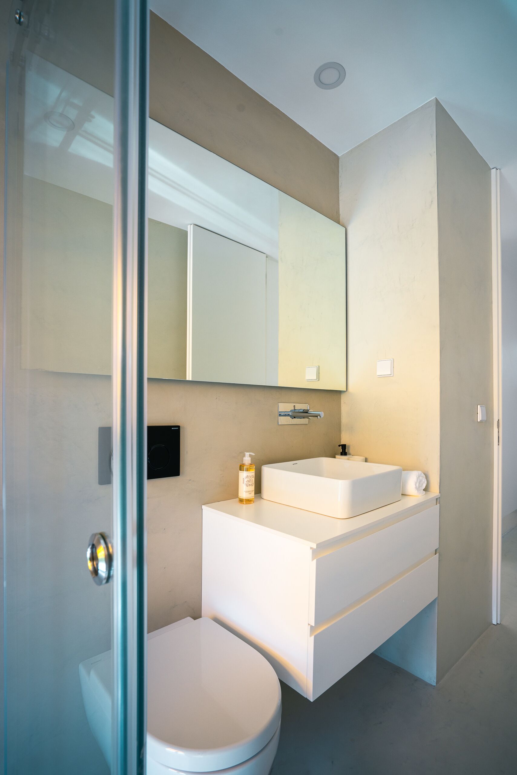 Ein modernes Badezimmer mit Glasdusche, weißer Toilette, Waschtisch mit Spiegel und Waschbecken.