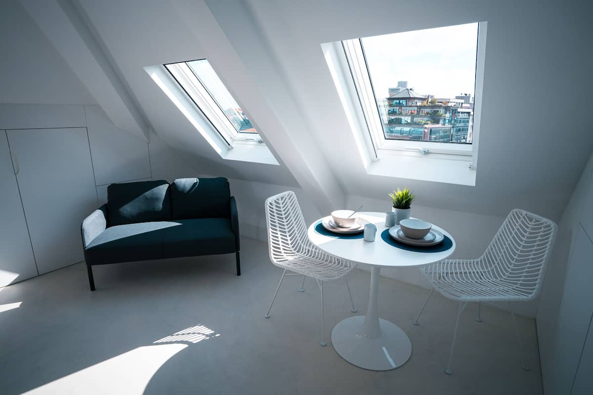Ett modernt sovrum i loftstil med takfönster, en säng, ett matbord med stolar och utsikt över staden.