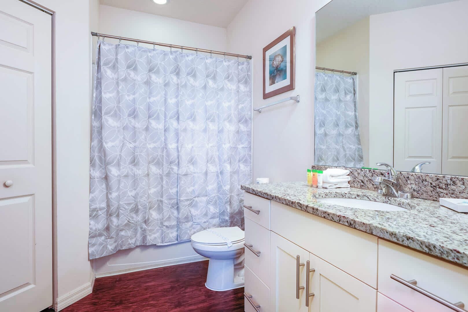 A bathroom with a toilet, a sink with a marble countertop, and a shower curtain with a geometric pattern.