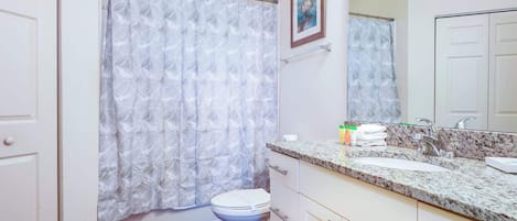 A bathroom with a toilet, a sink with a marble countertop, and a shower curtain with a geometric pattern.