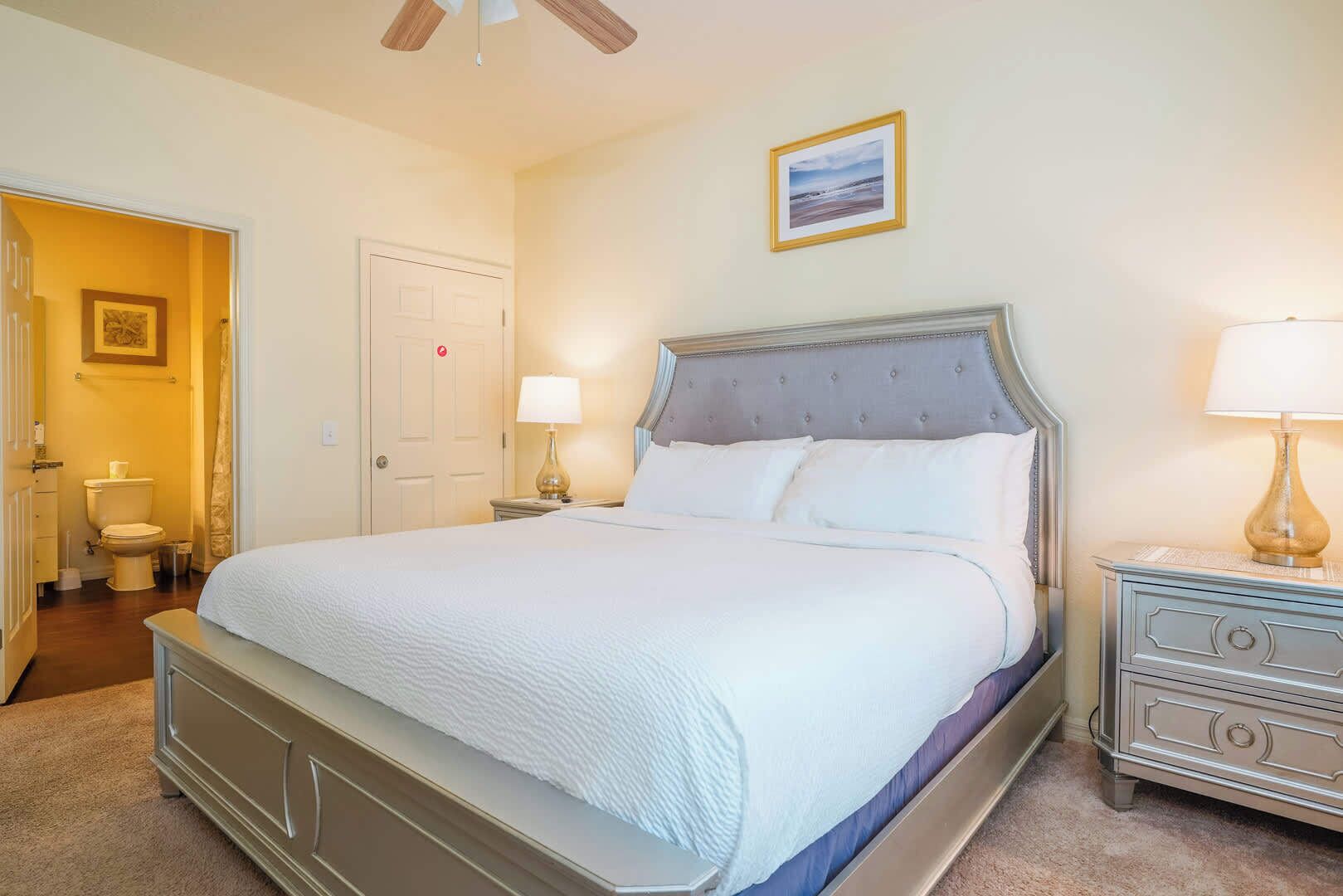 A neatly arranged bedroom with a large bed, bedside tables, a ceiling fan, and a framed picture on the wall.