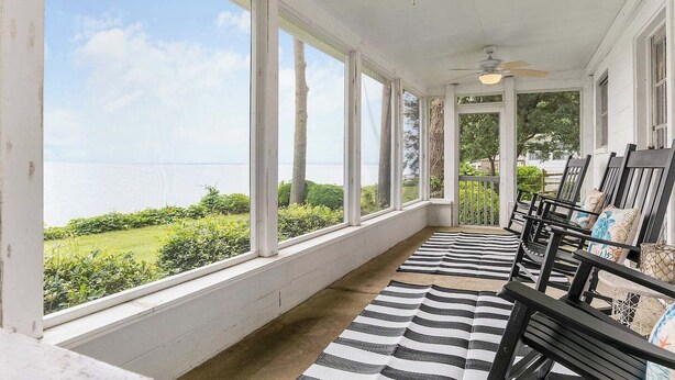 A covered porch with a view of the sea, wooden chairs, and a striped rug. - Riverfront Cottage w/ Private Beach Near Wmsburg (Surry)