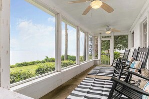 A covered porch with a view of the sea, wooden chairs, and a striped rug.