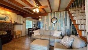 A cozy living room with a sectional sofa, a fireplace, and a wooden staircase. - Riverfront Cottage w/ Private Beach Near Wmsburg (Surry)