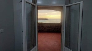 A room with a view of a sunset over water, a red carpet, and a door leading to another room. - Appartement F2 (Souk Tleta)