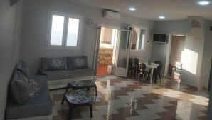 A living room with a sofa, a coffee table, and a dining area with chairs and a table. - Appartement F2 (Souk Tleta)