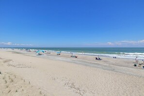 A wide sandy beach with umbrellas and beach chairs, a clear blue sky, and calm ocean waves.