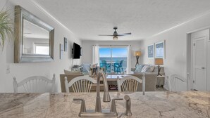 A modern kitchen with a marble countertop, a ceiling fan, and a view of the ocean through a sliding glass door. - Seaside Vista, Luxury Oceanfront, Top "2nd" Floor, Amazing Views!! (Kure Beach)